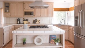 Una cucina moderna con pensili in legno chiaro, un'isola centrale con piano cottura, forno a microonde e frigorifero in acciaio inossidabile.