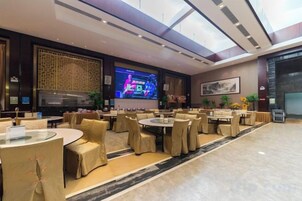 Un lobby espacioso de hotel con varias zonas de estar, una pantalla grande mostrando un programa y una decoración de interiores moderna.