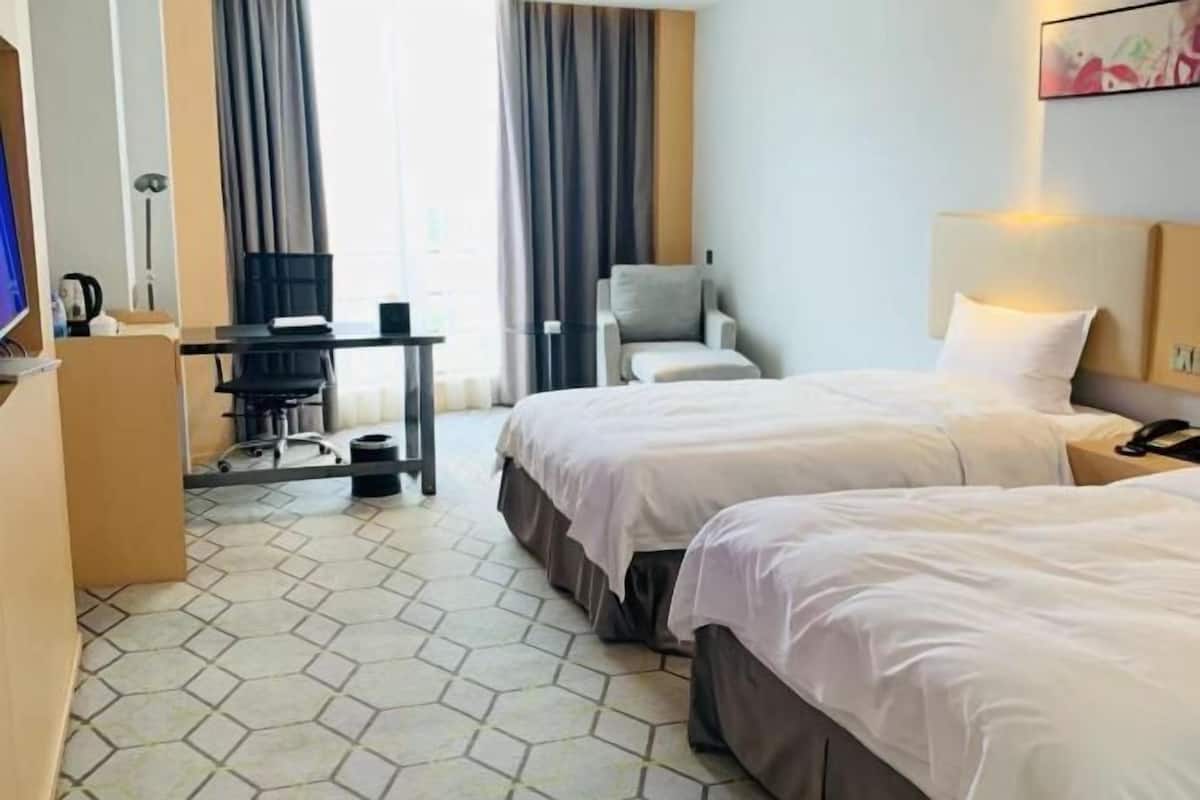 Une chambre d’hôtel avec deux lits, un bureau avec une chaise, une télévision et une fenêtre avec des rideaux.
