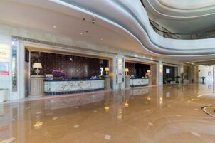 A spacious lobby with a marble reception desk, a high ceiling, and a polished floor.