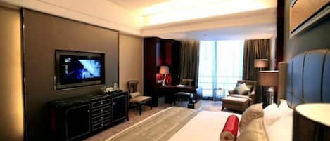 A hotel room with a large bed, a television, a desk, and a seating area with chairs and a sofa.