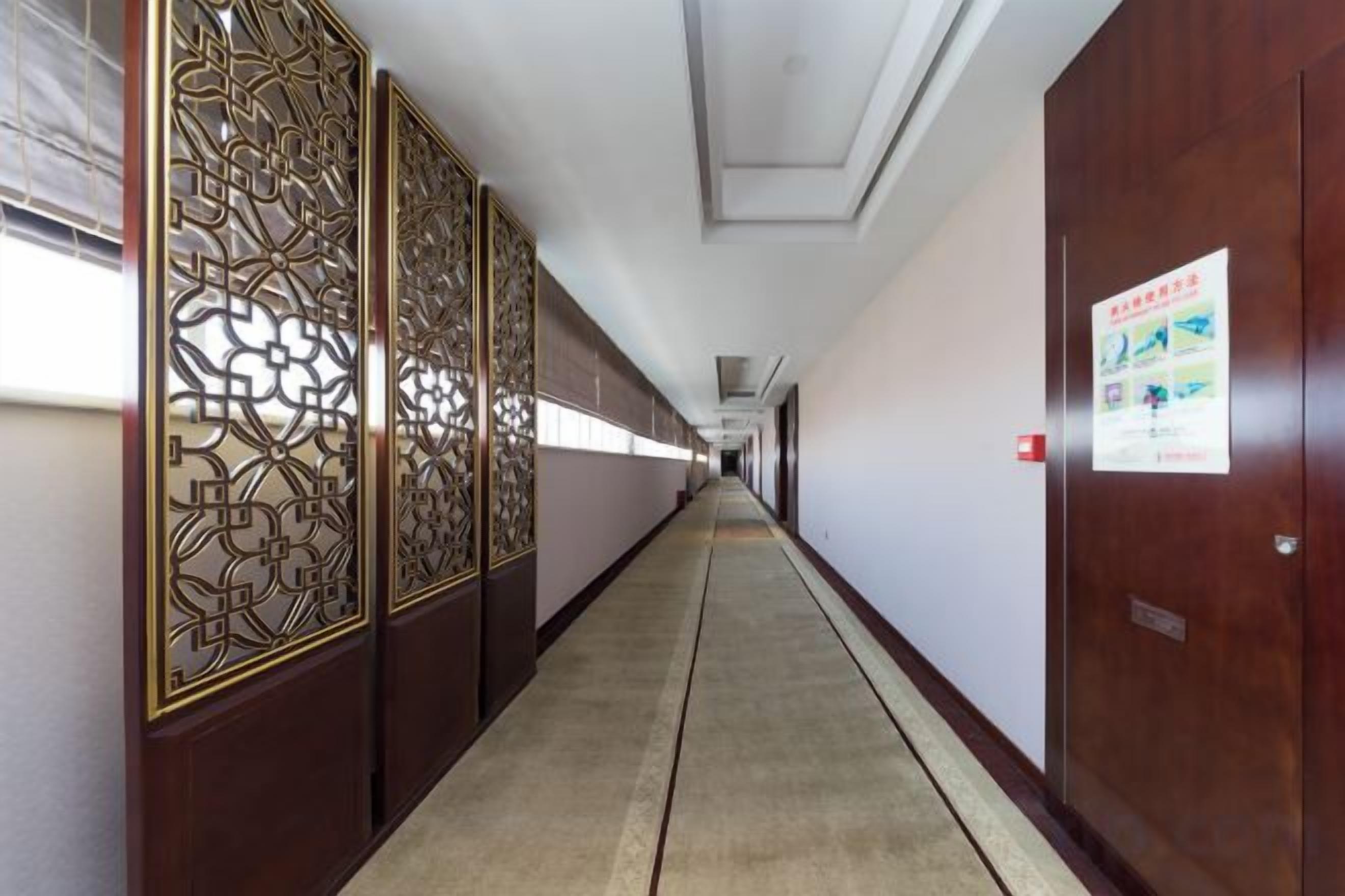 A corridor with a wooden door on the right, a poster on the wall, and a patterned screen on the left.