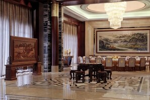 Un hall d’entrée avec un comptoir de réception, un espace repas avec des chaises et une table, un grand tableau au mur et un lustre.