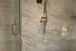 A glass-enclosed shower area with a marble wall and a showerhead.