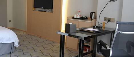 A hotel room with a bed, a desk with a chair, a television, and a trash bin.