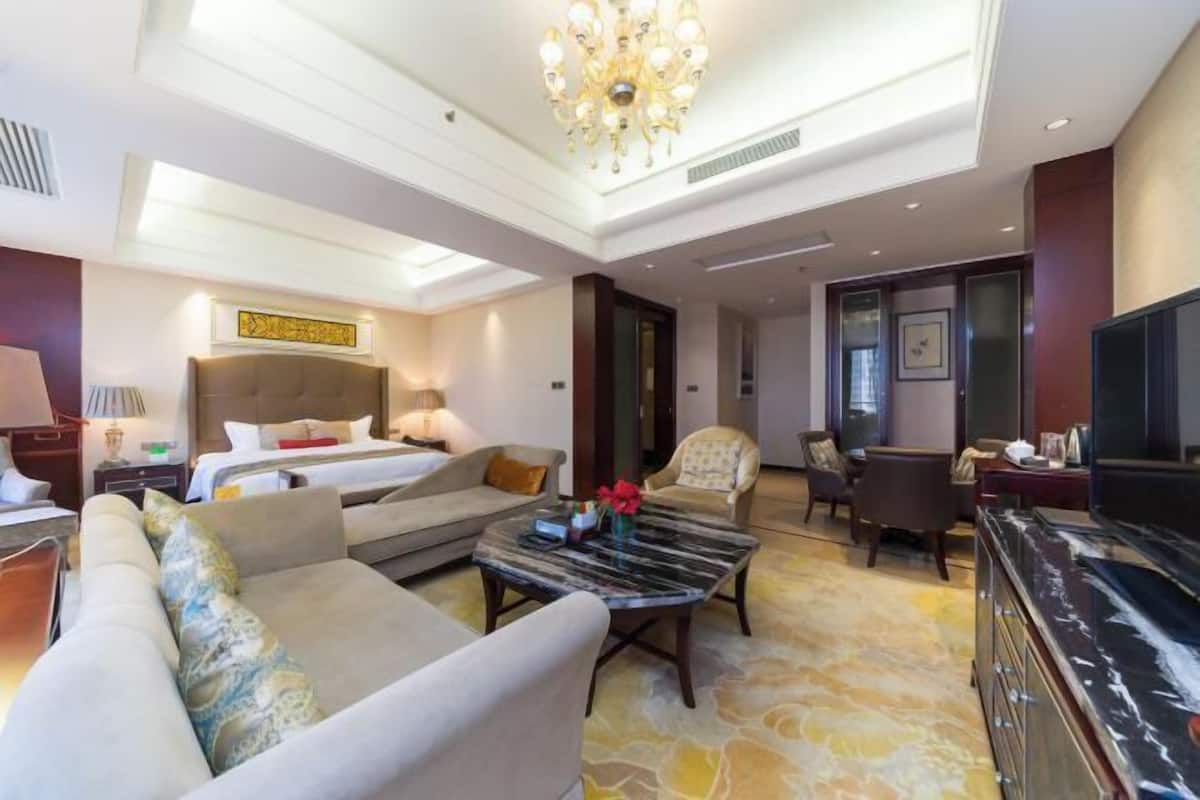 Une chambre d’hôtel comprenant un lit, un canapé, un fauteuil, une table basse, une télévision et un lustre.