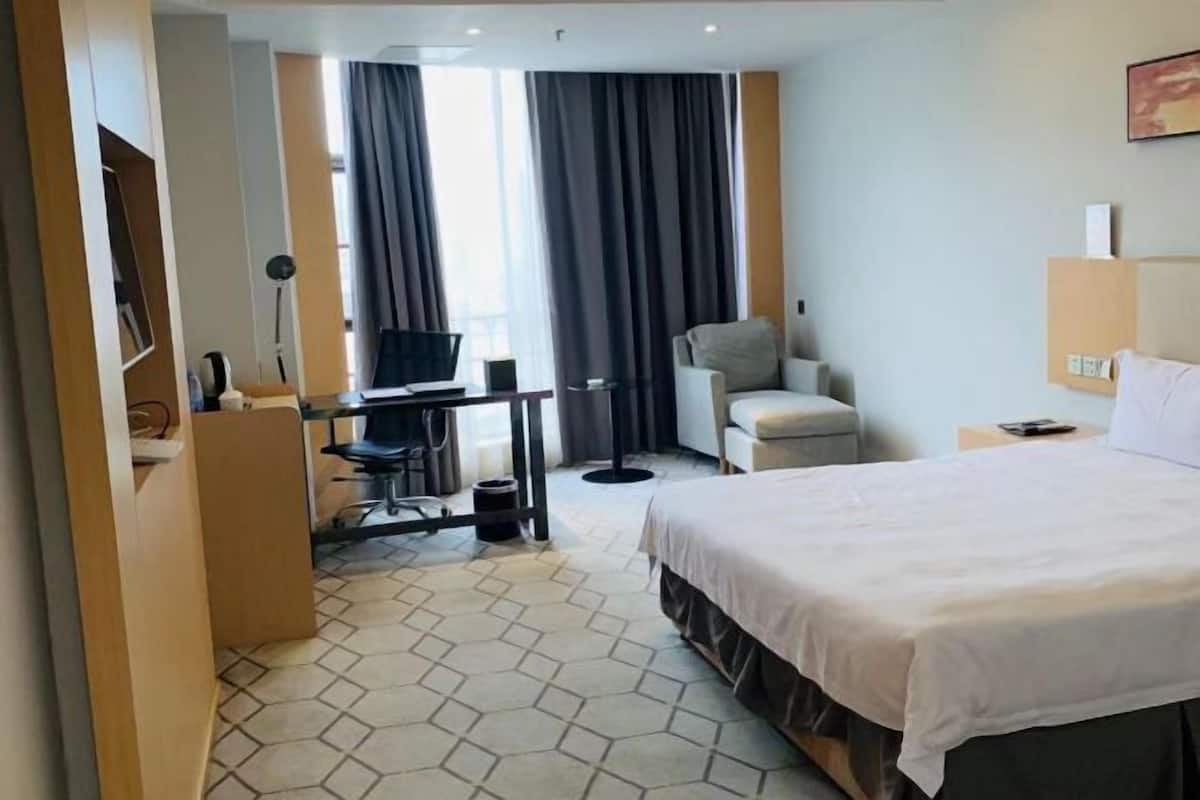 Une chambre d’hôtel avec un lit, un bureau avec un ordinateur, une chaise et une fenêtre avec des rideaux.