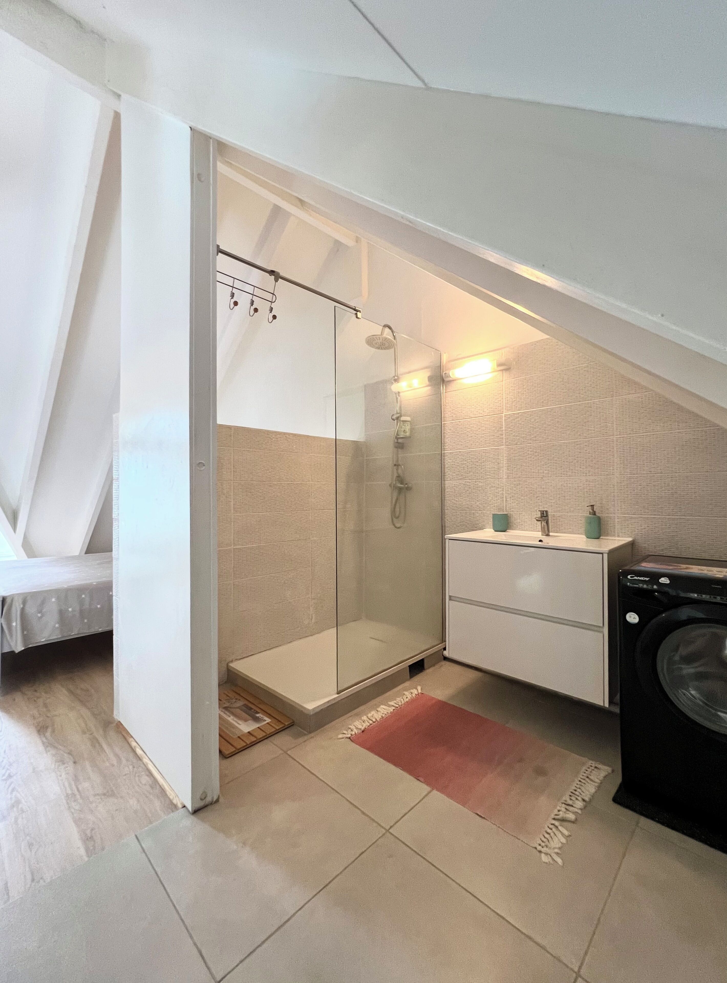 A compact bathroom with a glass-enclosed shower, a white sink with two soap dispensers, and a washing machine.
