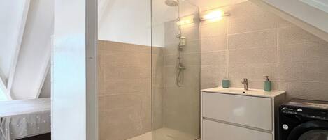 A compact bathroom with a glass-enclosed shower, a white sink with two soap dispensers, and a washing machine.