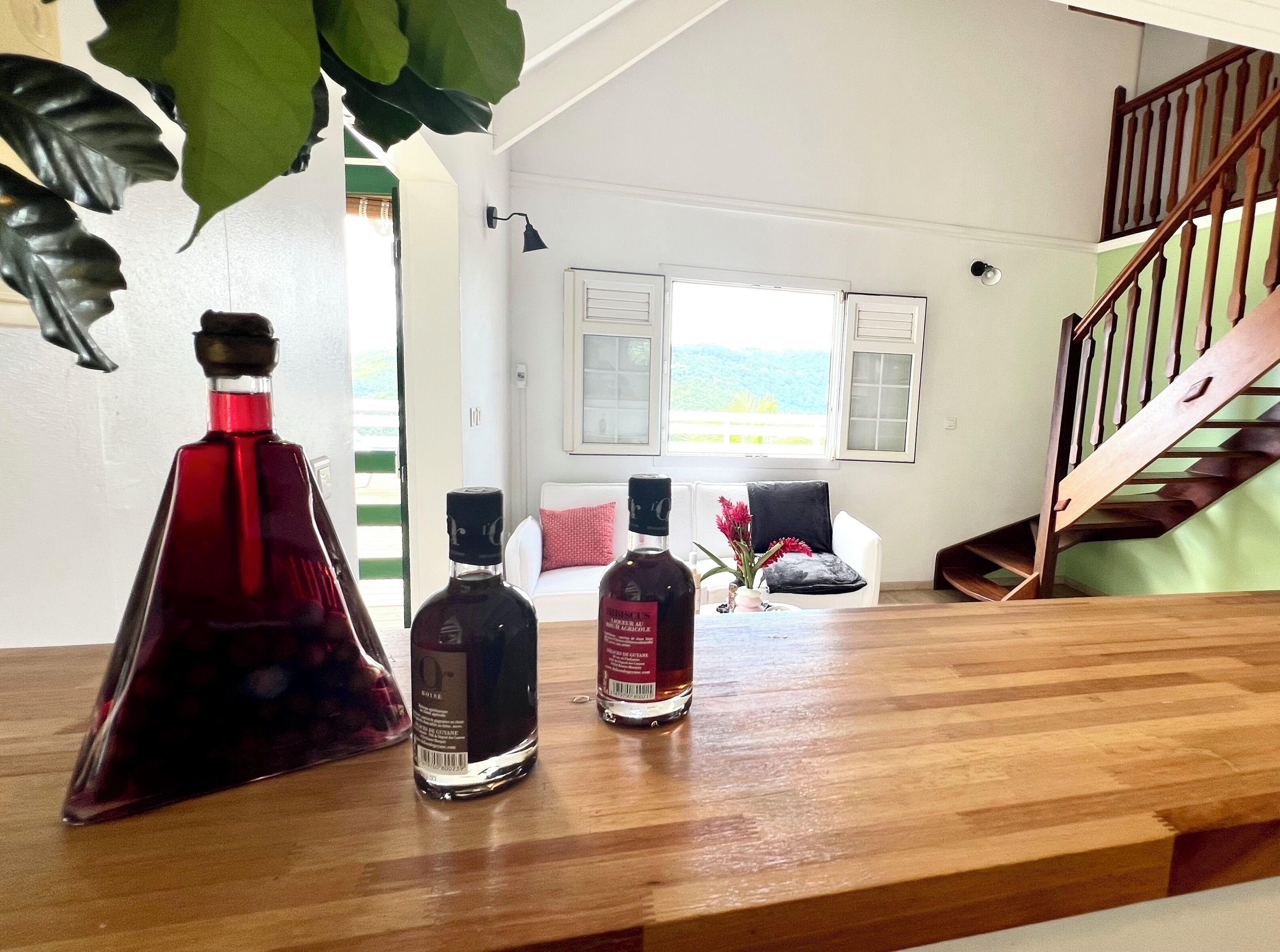 A wooden table with three bottles of liquor, a white sofa, and a staircase in the background.