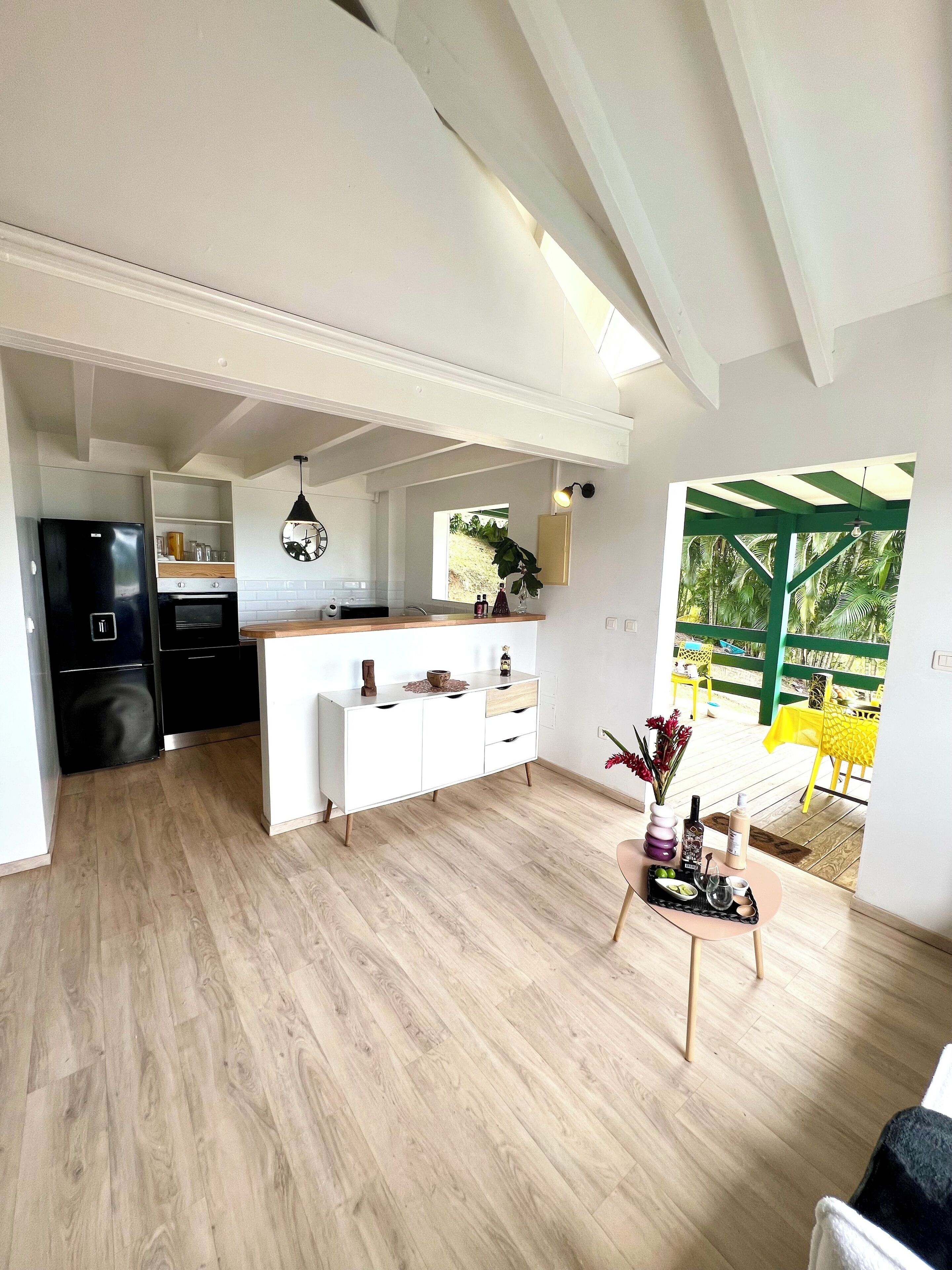 A modern kitchen with a central island, a dining area with a table and chairs, and a view of a green outdoor deck.