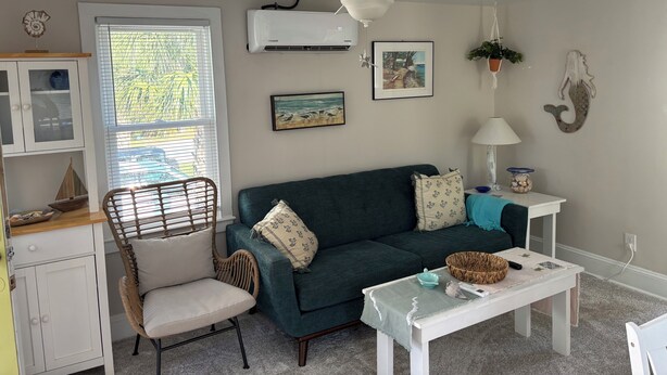 Un salon avec un canapé vert, une table blanche, un fauteuil en osier et un ventilateur de plafond.