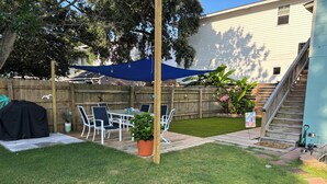 Un jardin avec une terrasse, du mobilier d’extérieur, un barbecue et une clôture en bois.