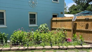Une maison à l’extérieur bleu, avec une clôture en bois et un jardin où poussent différentes plantes et fleurs.