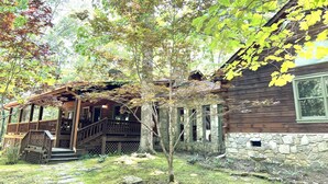 Une cabane rustique avec des fondations en pierre, une terrasse en bois et un porche abrité.