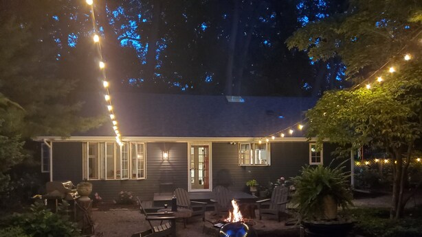 A house with a patio area featuring outdoor furniture, a fire pit, and string lights. - Beautiful Private Cottage, Sleeps 6, Walk to Beach (New Buffalo)