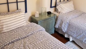 A bedroom with two beds, each with a striped headboard and matching bedding. There is a small table with a lamp and a radio between the beds. - Beautiful Private Cottage, Sleeps 6, Walk to Beach (New Buffalo)