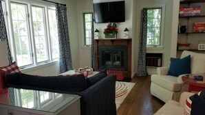 A living room with a sofa, a white armchair, a glass-top table, and a fireplace. - Beautiful Private Cottage, Sleeps 6, Walk to Beach (New Buffalo)