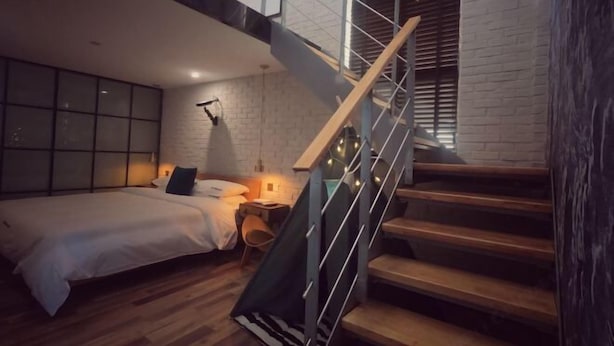 A bedroom with a bed, bedside table, lamp, and a staircase with wooden steps and metal railings. - Punk Ballet Ins Hotel (Changzhou Dinosaur Park) (Changzhou)