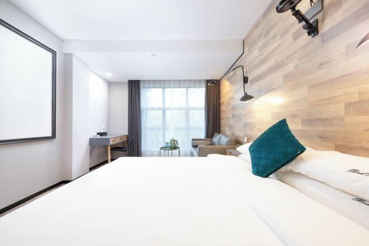 A hotel room with a large bed, a desk, a chair, and a window with curtains.