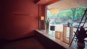 A modern reception area with a red wall, a large window with a view of the street, and a hanging light fixture. - Punk Ballet Ins Hotel (Changzhou Dinosaur Park) (Changzhou)