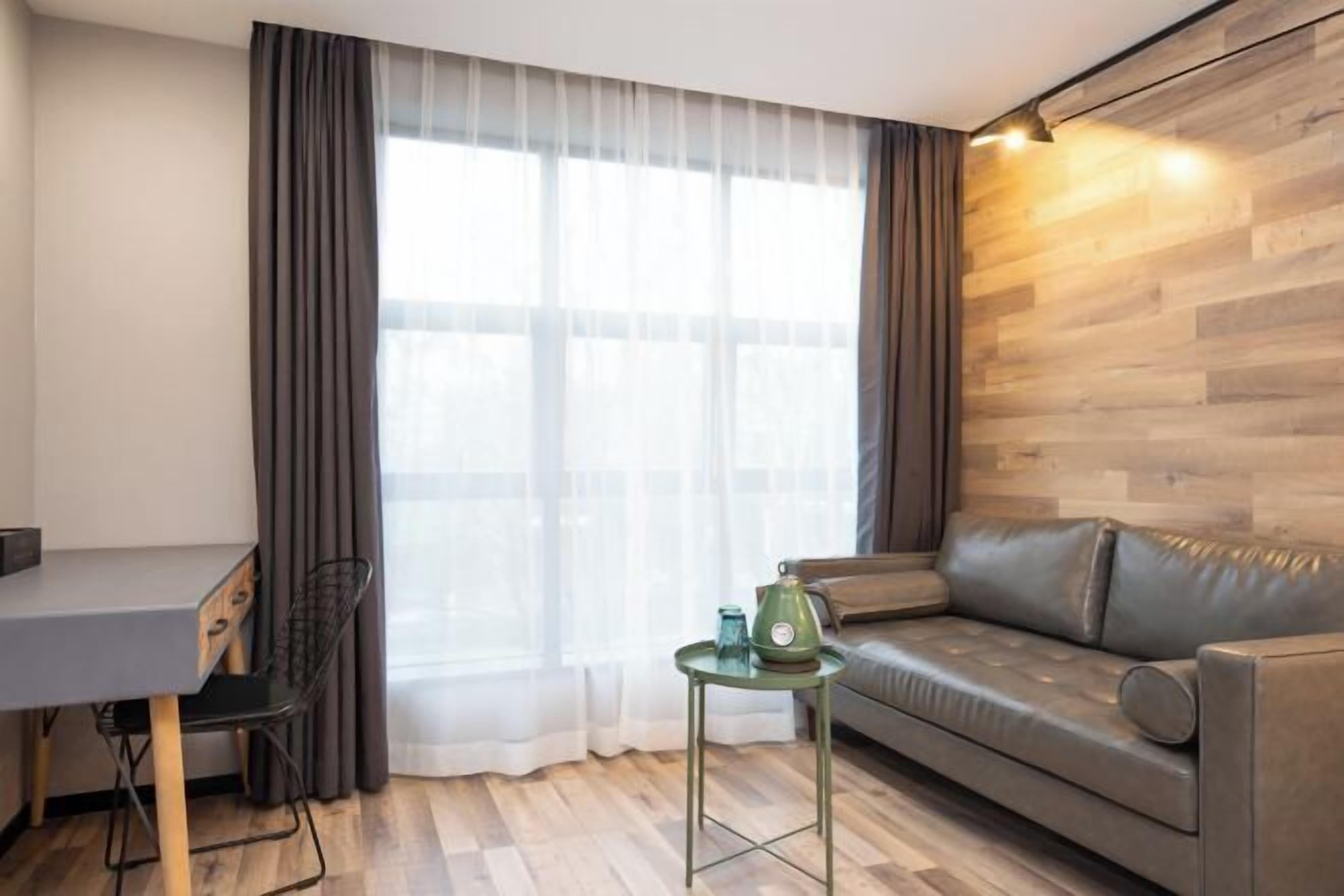 Una sala de estar moderna con un sofá gris, una mesita con una lámpara verde y un escritorio con una silla.