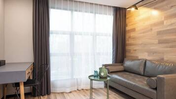 Una sala de estar moderna con un sofá gris, una mesita con una lámpara verde y un escritorio con una silla.