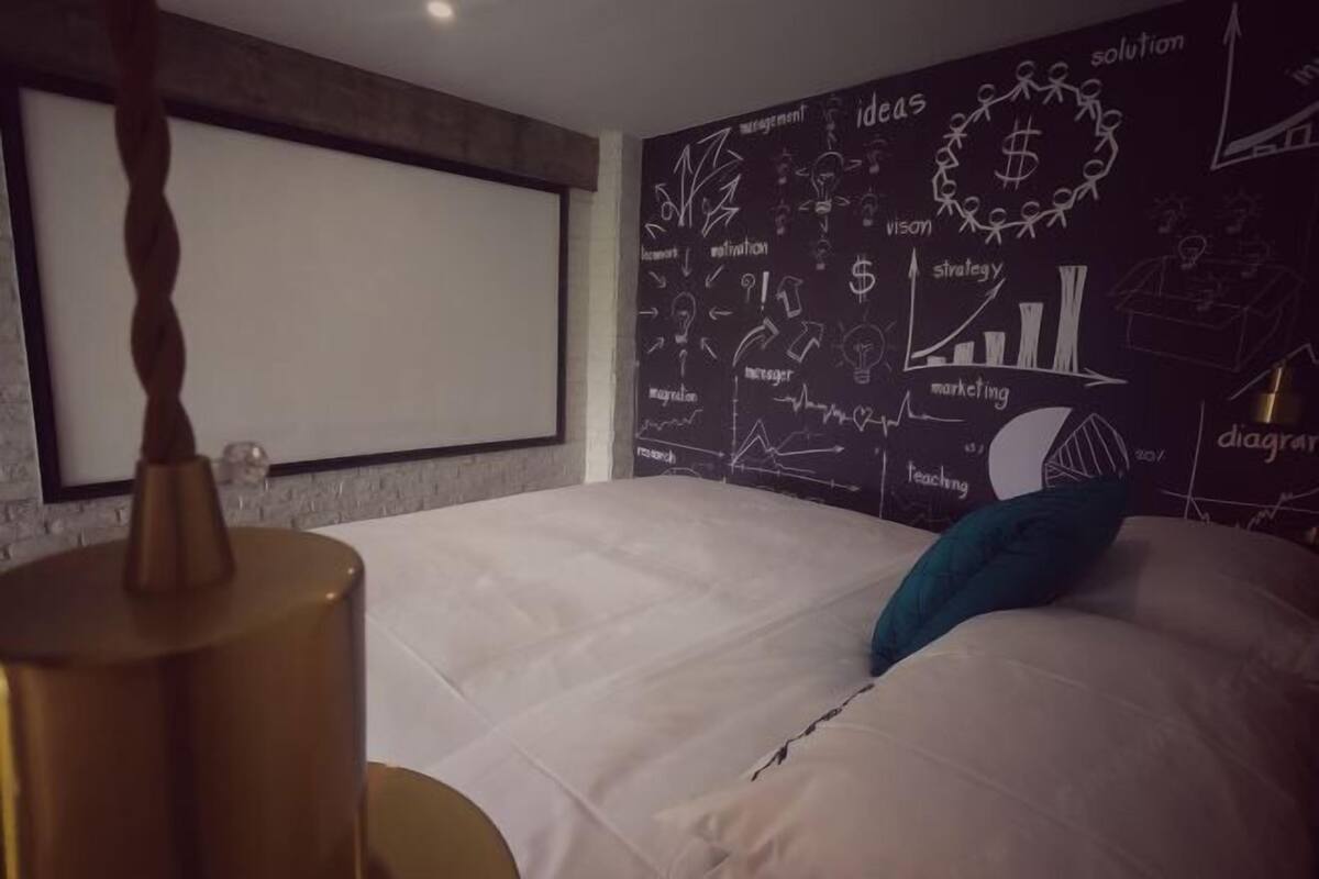 A bedroom with a bed, a wall-mounted projector screen, and a chalkboard wall with business-related drawings.