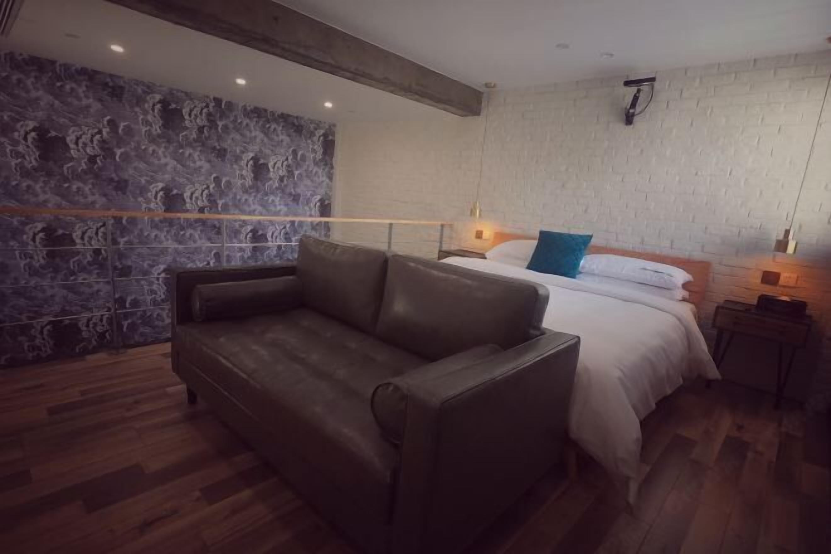 Ein Schlafzimmer mit einem Bett, einem braunen Ledersofa, einer Steinwand und einem Holzboden.