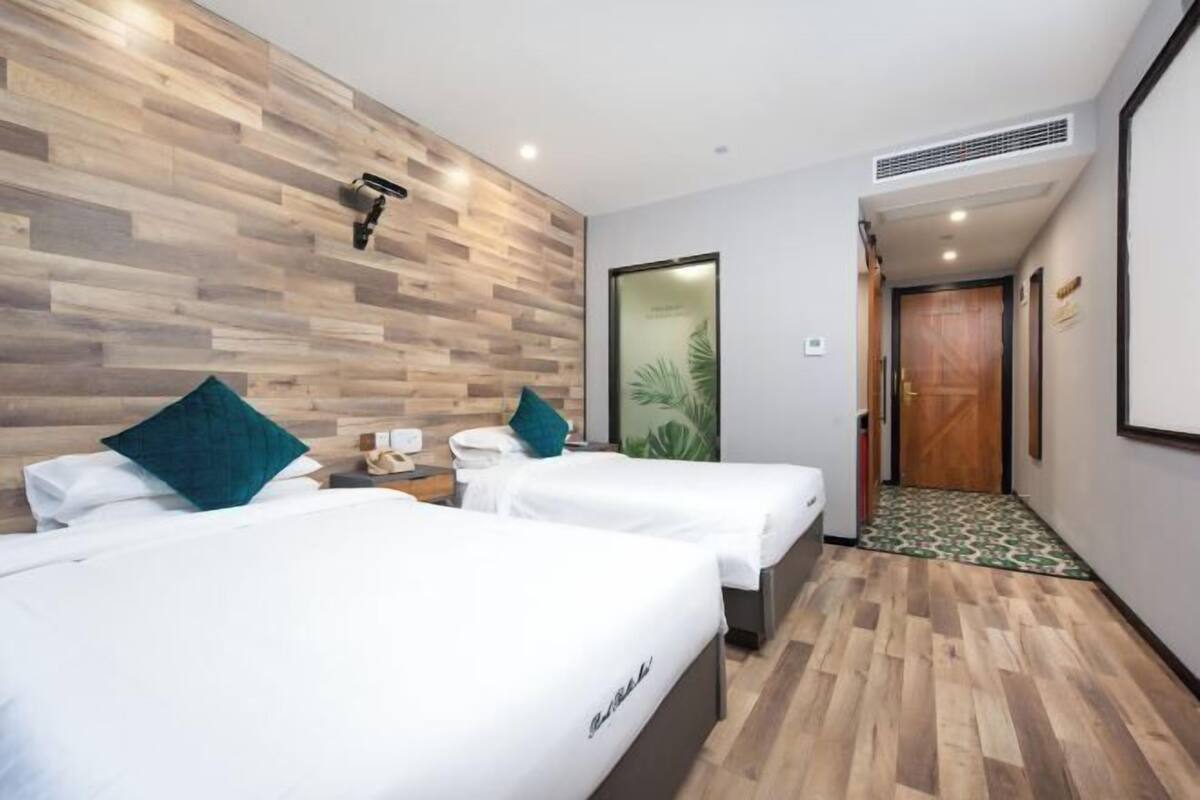 A hotel room with two beds, a wooden wall, a door, and a small table with a lamp.