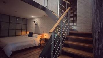 Un dormitorio con cama, mesita de noche, lámpara y una escalera con barandilla.