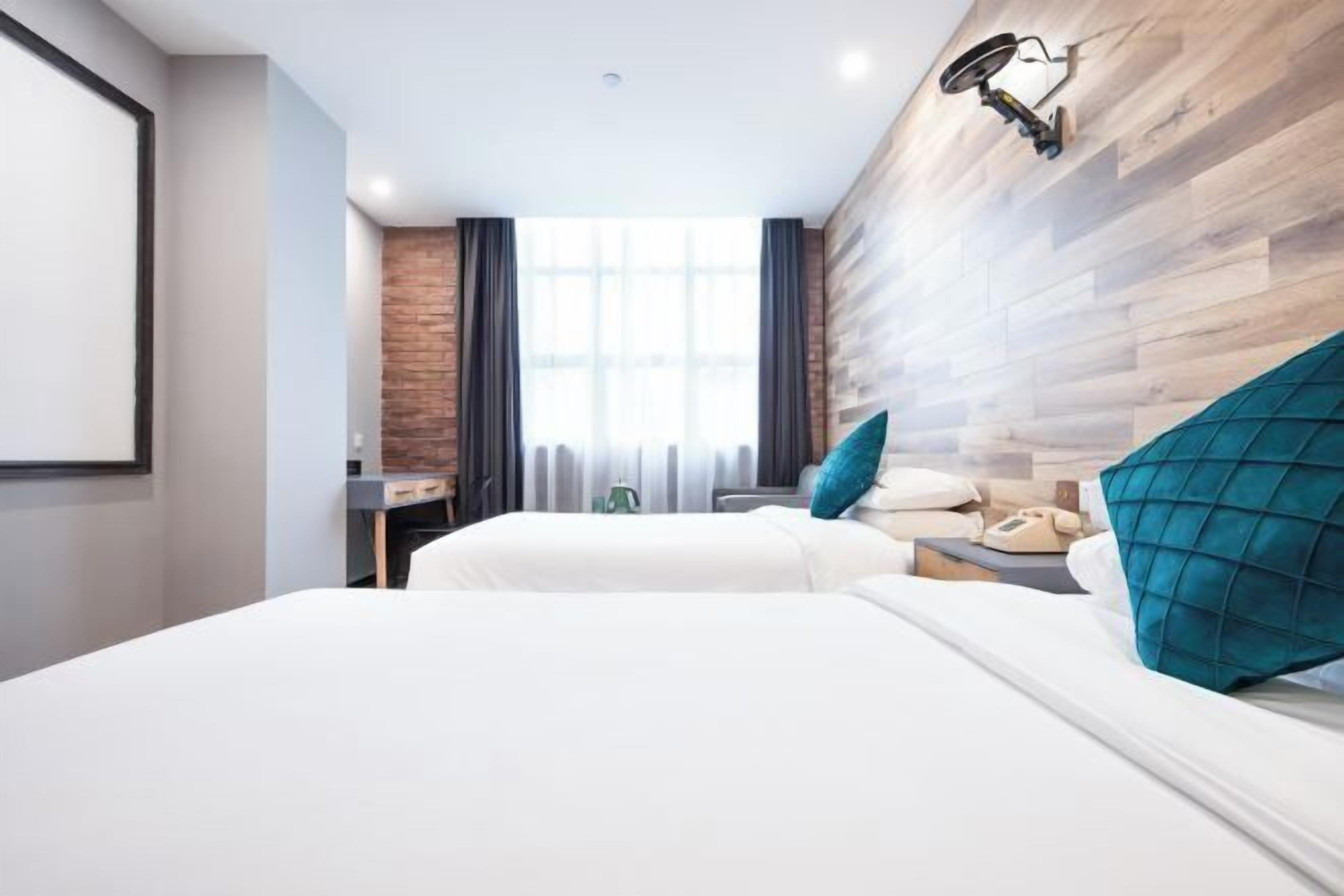 Une chambre d’hôtel avec deux lits, un bureau, une chaise, une lampe et une fenêtre avec des rideaux.