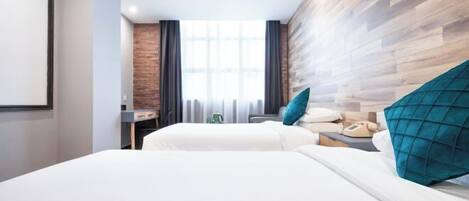 A hotel room with two beds, a desk, a chair, a lamp, and a window with curtains.