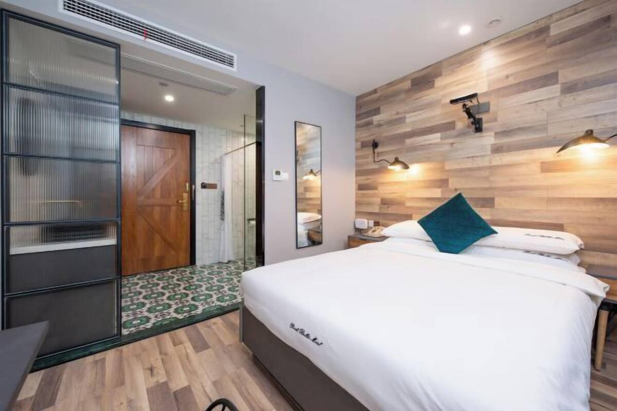 A modern hotel room with a bed, a nightstand, a mirror, and a wooden wall panel.