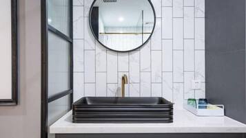 A bathroom with a white tiled wall, a round mirror, a black sink, and a gold faucet.