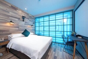 A modern bedroom with a wooden wall, a large window with blue lighting, a bed with white linens, a desk with a chair, and a nightstand with a lamp. - Punk Ballet Ins Hotel (Changzhou Dinosaur Park) (Changzhou)