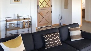 A living room with a black sofa, a wooden door, and a macrame wall hanging. - Peaceful mid-century house under the boulders near Joshua Tree National Park (Joshua Tree)
