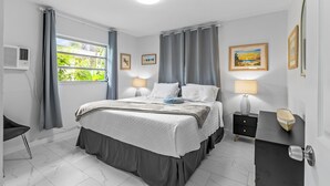 A bedroom with a bed, bedside tables, a dresser, a window with curtains, and wall art. - KEYLIME COTTAGE Heated Pools, steps from the beach perfect location (Clearwater)