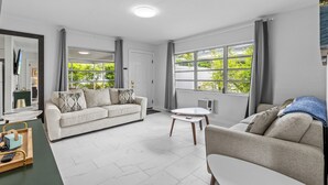 A modern living room with a sofa, a coffee table, and a view of greenery outside. - KEYLIME COTTAGE Heated Pools, steps from the beach perfect location (Clearwater)