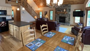 Un vaste espace de vie doté d’un plafond en bois, d’une cheminée en pierre et d’une table à manger avec des sets de table.