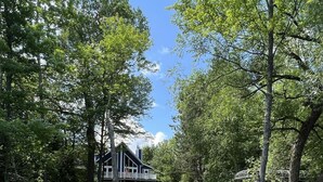 Une jetée s’avançant dans une étendue d’eau calme, entourée d’une végétation luxuriante et d’une grande maison dotée d’un balcon.