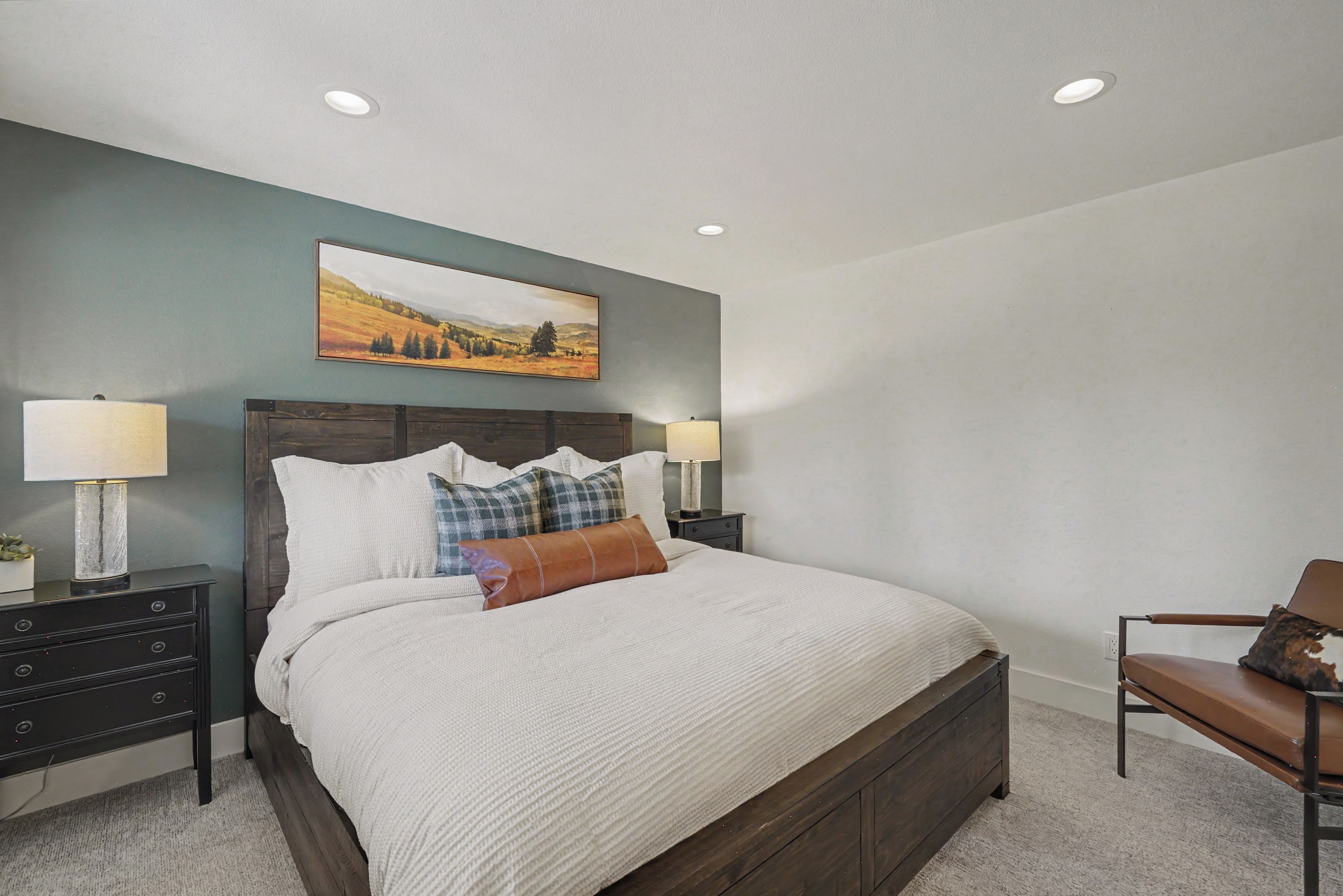 A bedroom with a bed, two bedside tables, a nightstand, a chair, and a painting on the wall.