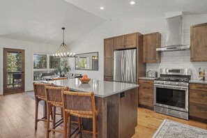 A modern kitchen with a central island, wooden cabinets, stainless steel appliances, and a chandelier.