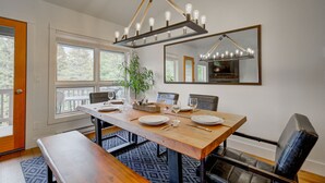 Un coin repas avec une table en bois dressée pour quatre personnes, un luminaire suspendu et un grand miroir au mur.