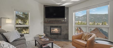Una sala de estar moderna con chimenea, un televisor de pantalla plana y ventanas amplias que ofrecen vistas al exterior.