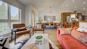 Un salon spacieux doté d’une grande fenêtre, d’un canapé, d’une table basse et d’un coin repas agrémenté d’un lustre.