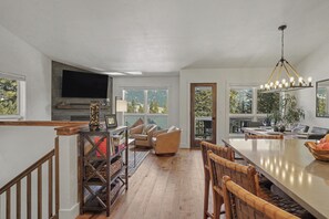 A spacious kitchen with a large island, a dining area with wooden chairs, a fireplace, and a television mounted on the wall.