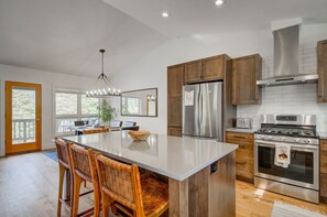 Une cuisine moderne dotée d’un grand îlot central, de meubles en bois, d’appareils électroménagers en acier inoxydable et offrant une vue sur l’extérieur.