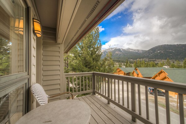 Une terrasse en bois avec une table et des chaises, offrant une vue sur un paysage montagneux parsemé de chalets.