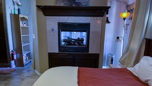 A bedroom with a bed, a fireplace, a television, and a nightstand.